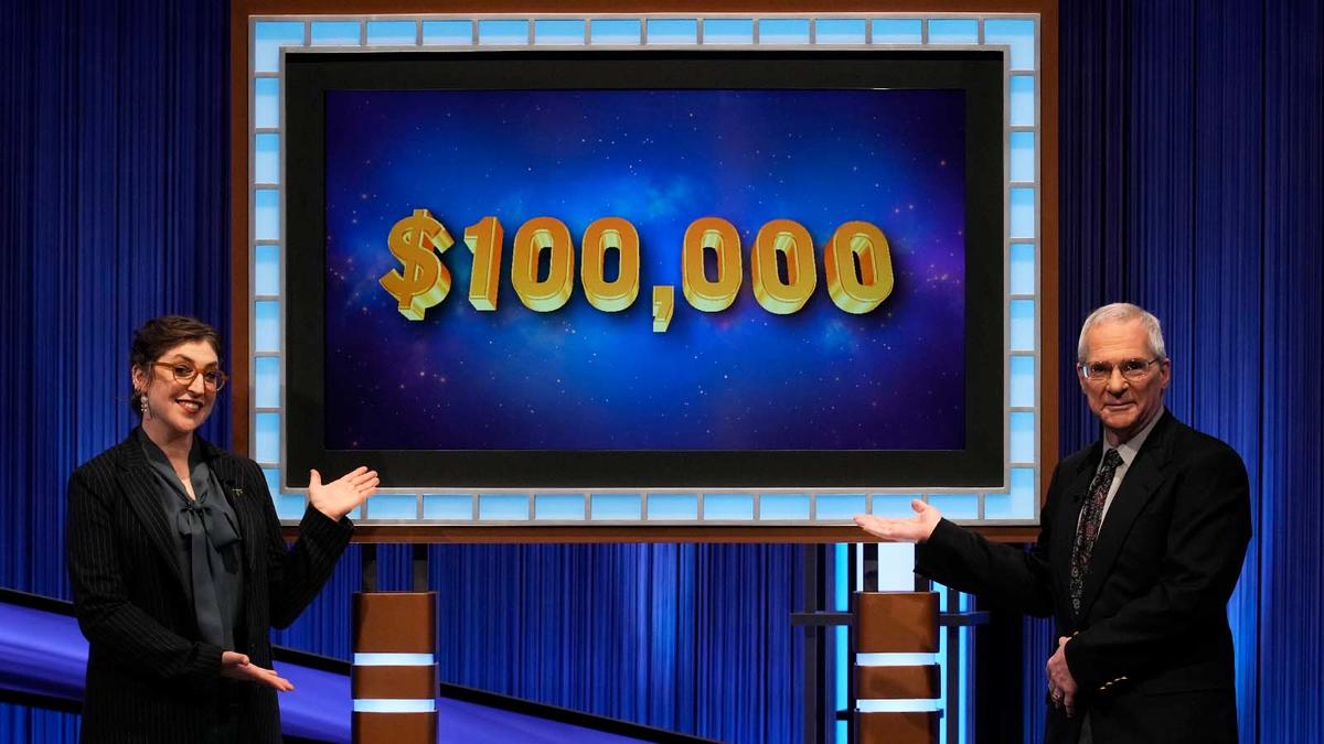 Mayim Bialik and Sam Buttrey in front of the screen that says $100,000