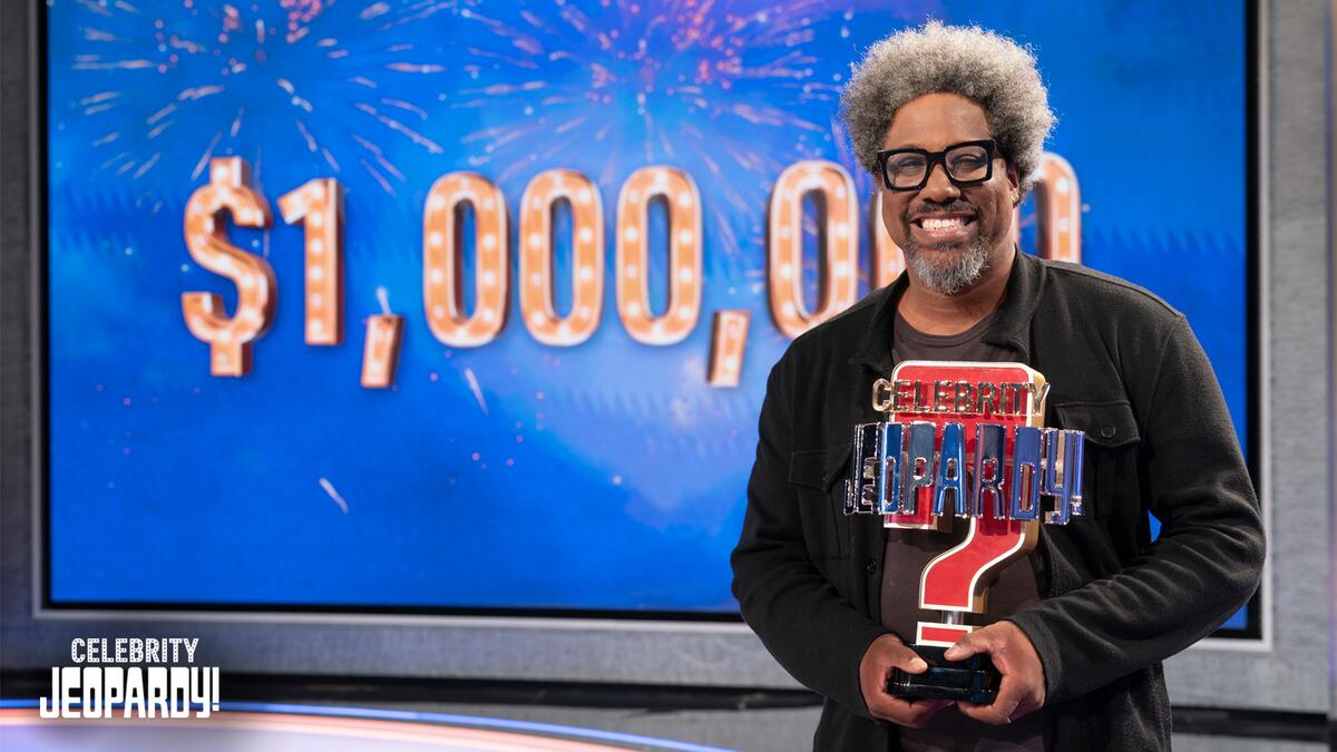W. Kamau Bell holding his Celebrity Jeopardy! trophy. 