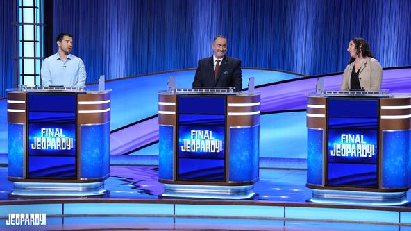 Cris Pannullo, Michael Harten, and Xanni Brown behind the contestant podiums on set. 